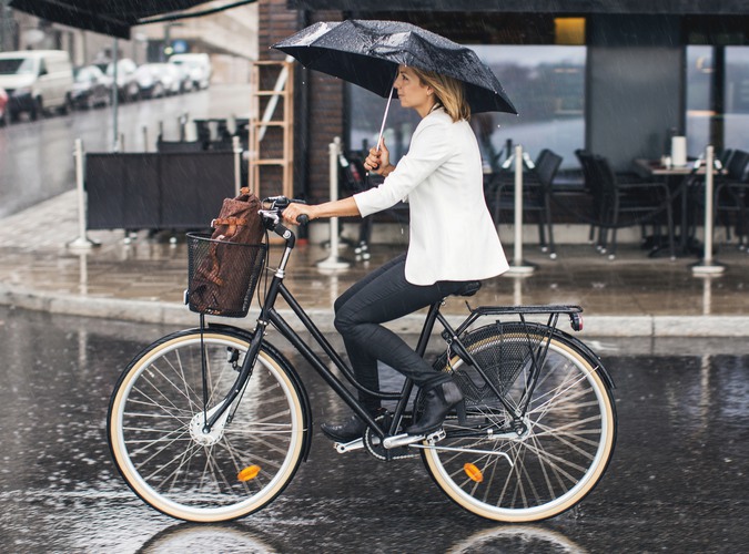 Kvinna cyklar i regnet. Håller samtidigt i ett paraply.