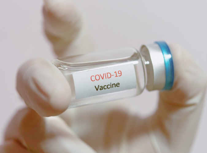 En hand med plasthandske håller en glasflaska med vaccin mot covid-19. Vaccine COVID-19 (Coronavirus) glass bottle in medical doctor hand