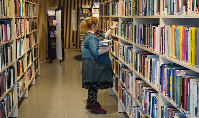 På bilden syns en kvinnlig bibliotekarie som ställer in böcker i en bokhylla.